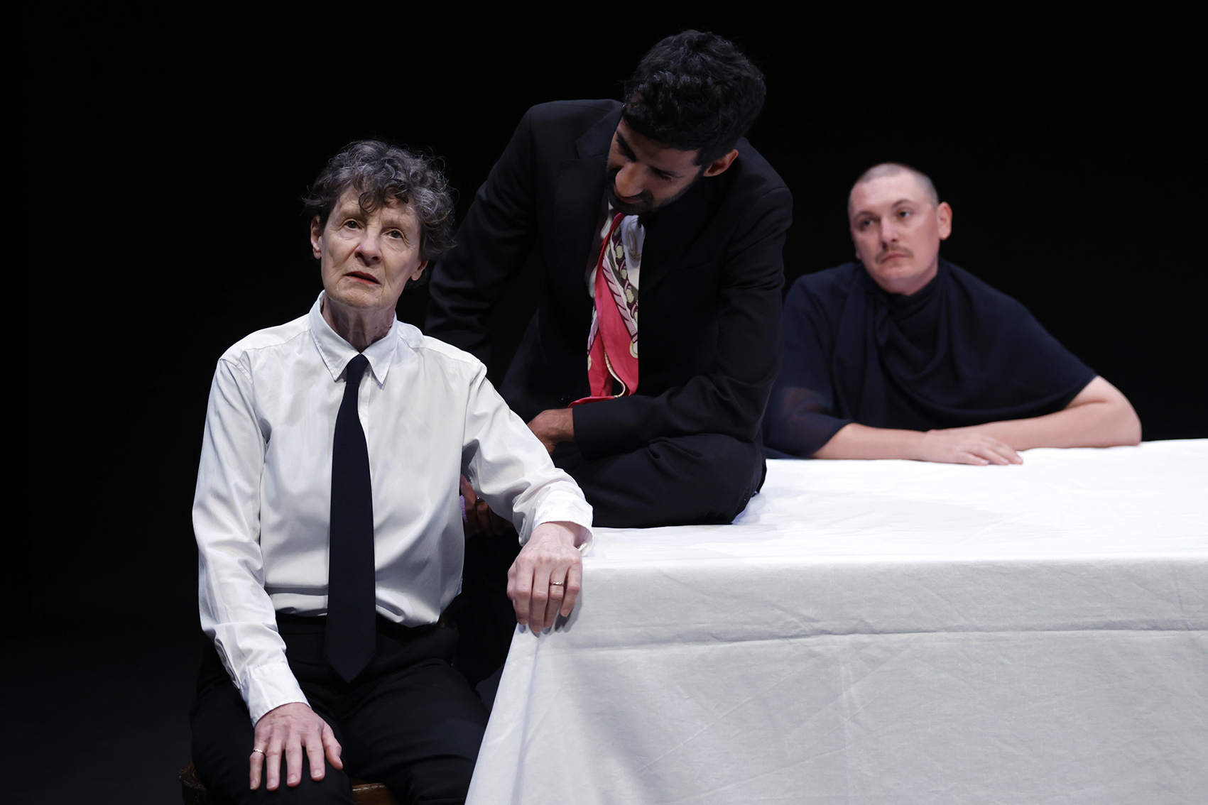 Three actors sitting at a table, one crying