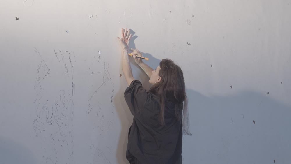 Jimena holding her left arm up against a white wall and drawing on it with her right hand